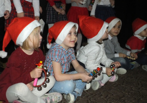 kilkoro dzieci siedzi na dywanie i śpiewa Mikołajowi piosenki