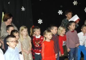 grupa dzieci stoi i śpiewa Mikołajowi piosenkę
