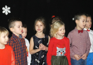 kilkoro dzieci stoi i śpiewa Mikołajowi piosenkę