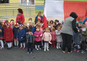 dzieci i pracownicy stoją przed budynkiem, przygotowują się do śpiewania hymnu