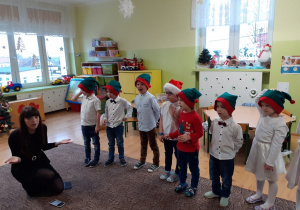 dzieci w czapeczkach elfów spiewają po angielsku świąteczne piosenki, obok kuca lektorka