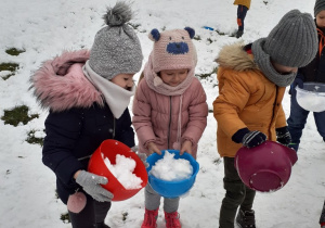 troje dzieci stoi na dworze, w rękach trzymają miski ze śniegiem