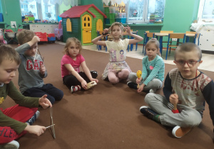 grupa siedzi w kole na dywanie, dzieci mają w rękach rózne instrumenty