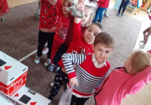 grupa dzieci ubranych na czerwono stoi w kolejce, by wrzucić do specjalnego pojemnika zużyte baterie