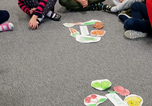 dzieci na podłodze oglądają papierowe emblematy owoców
