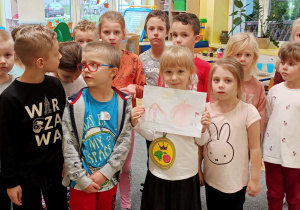 grupa dzieci, w środku dziewczynka prezentuje swoją pracę plastyczną