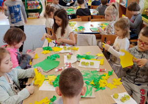 dzieci siedzą przy stoliku i wyklejają z kolorowego papieru