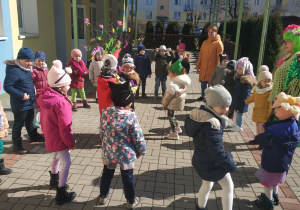 grupa dzieci tańczyw przedszkolnym ogrodzie, uczestniczy w powitaniu wiosny