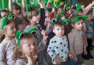 grupa dzieci stoi w szatni bierze udział w zabawie ruchowej. Na głowach mają opaski zajączki i opaski żabki