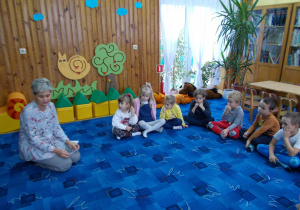 bibliotekarka i grupa dzieci siedzi na dywanie w czytelni