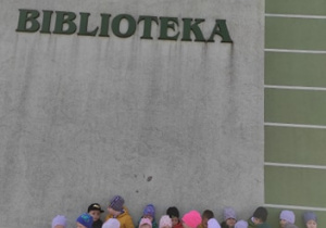 Grupa "Biedronki" stoi przy budynku z napisem "BIBLIOTEKA"