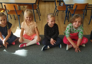pięcioro dzieci siedzi na dywanie, bierze udział w zajęciach