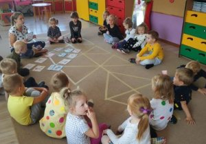 grupa dzieci siedzi na dywanie, z nimi nauczycielka, która mówi do nich