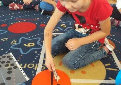 dziewczynka siedzi na dywanie i wykonuje matematyczne zadanie : kropki biedronki, za nią troje dzieci
