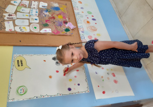 dziewczynka, ubrana w sukienkę w kropki, rysuje kropkę na papierze przyklejonym do ściany w szatni