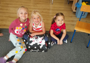 trzy dziewczynki, w ubraniach w kropki siedzą na dywanie w klasie
