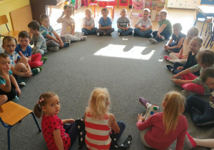 grupa dzieci siedzi w kole na dywanie, uczestniczą w zajęciach