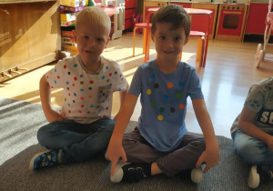 trzech chłopców, w ubraniach w kropki siedzi na dywanie w klasie
