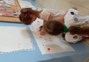 dwie dziewczynki ryzują kropki na papierze przyczepionym do ściany w szatni