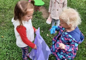 trzy dziewczynki w ogrodzie przedszkolnym, jedna trzyma worek na śmieci