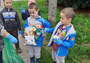 kilku chłopców trzyma w rękach znalezione śmieci , obok nauczycielka trzyma zielony worek