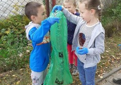 troje dzieci na dworze, dwoje trzyma zielony worek na odpady