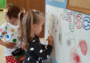 dziewczynka rysuje kropkę na papierze przyklejonym do ściany szatni