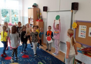dzieci w zabawie ruchowej przemieszczają się podywanie w klasie, dziewczynka podnosi w górę zielone koło