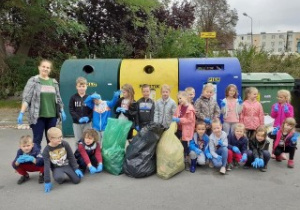 grupa dzieci pozuje do zdjęcia, przed nimi leżą worki z zebranymi śmieciami, za dziećmi kontenery na odpadki