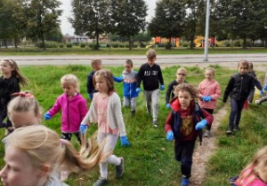 grupa dzieci na trawniku zbiera śmieci