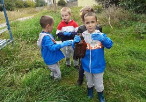 czworo dzieci stoi na trawie w rękach trzymają śmieci