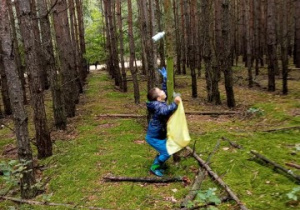 las, chłopiec podskakuje przy drzewie, by strącić plastikową butelkę, którą ktoś powiesił na gałęzi