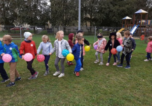 grupa dzieci z balonami w dłoniach tańczy w rytm muzyki na przedszkolnym podwórku
