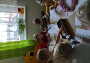 grupa dzieci siedzie przy stoliku, kolorują obrazki