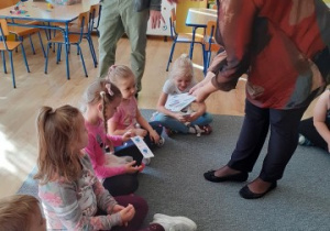 prowadząca zajęcia podchodzi do dzieci siedzących na dywanie, pokazuje im wynik eksperymentu , jaki przeprowadziła