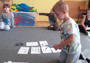dziec isiedzą na dywanie, jeden z chłopców segreguje obrazki przyporządkowując je do czarnej, lub białej chmurki