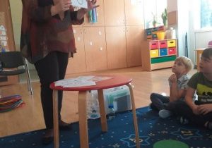 prowadząca warsztaty pokazuje dzieciom rysunek z fajką, na dywanie siedzi dwóch chłopców