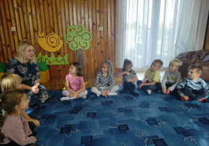 dzieci siedzą na dywanie w bibliotece, wśród nich pani bibliotekarka - czyta dzieciom