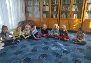 dzieci siedzą na dywanie w bibliotece, słuchają pani bibliotekarki, która czyta dzieciomczyta dzieciom