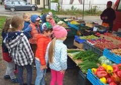 dzieci na dworze, stoją przy prawdziwym straganie z warzywami i owocami