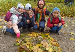 grupa dzieci kuca, przed nimi wykonana z liści mandala