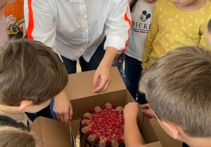 nauczycielka otwiera pudełko z tortem, obok stoją dzieci