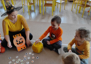 dzieci i nauczycielka siedzą na dywanie , grają w grę rzucając kostką