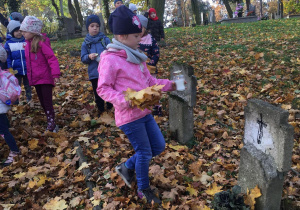 grupa dzieci na cmentarzu, dziewczynka trzyma w rękach liście i znicz