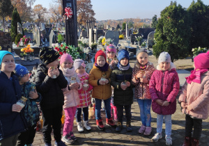 grupa dzieci na cmentarzu, w dłoniach trzymają znicze