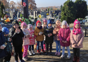 grupa dzieci na cmentarzu, w dłoniach trzymają znicze