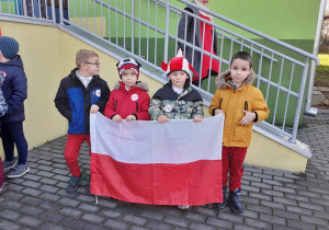 czterech chłopców na dworze, w rękach trzymają flagę