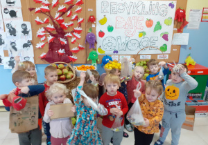 grupa dzieci pozuje do zdjęcia, w rękach mają owoce, za nimi plakat promujący akcję