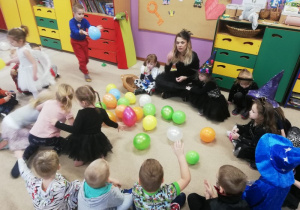 dzieci i nauczycielka przebrana za czarownicę siedzą w kręgu na dywanie, między nimi leżą kolorowe balony