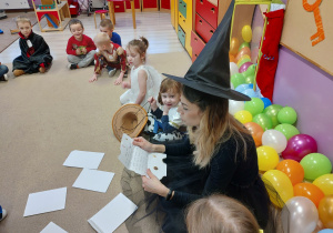 dzieci i nauczycielka przebrana za czarownicę siedzą w kręgu na dywanie, nauczycielka czyta list do dzieci